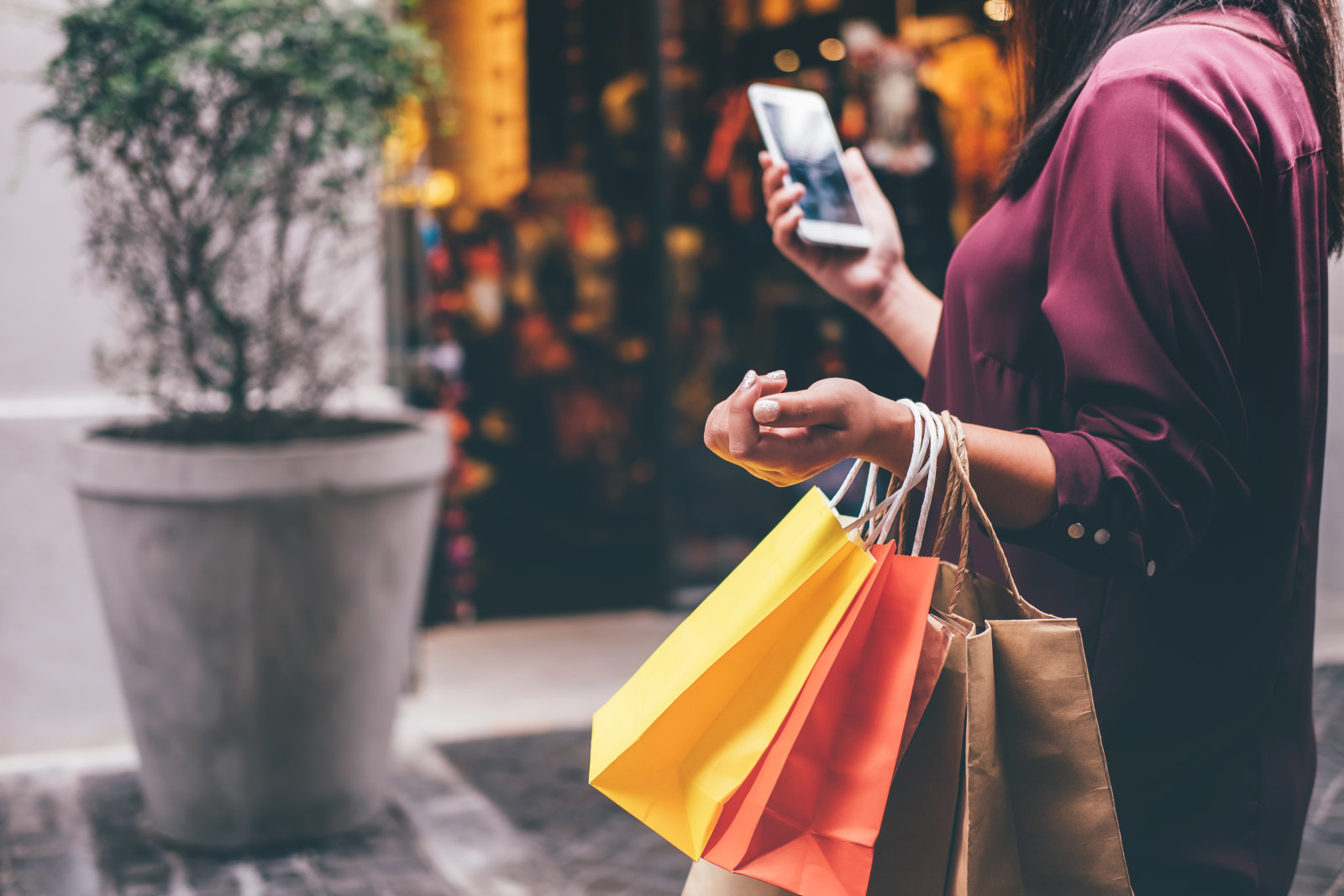 Midsection Of Woman Carrying Shopping Bags While Using Mobile Phone On Street